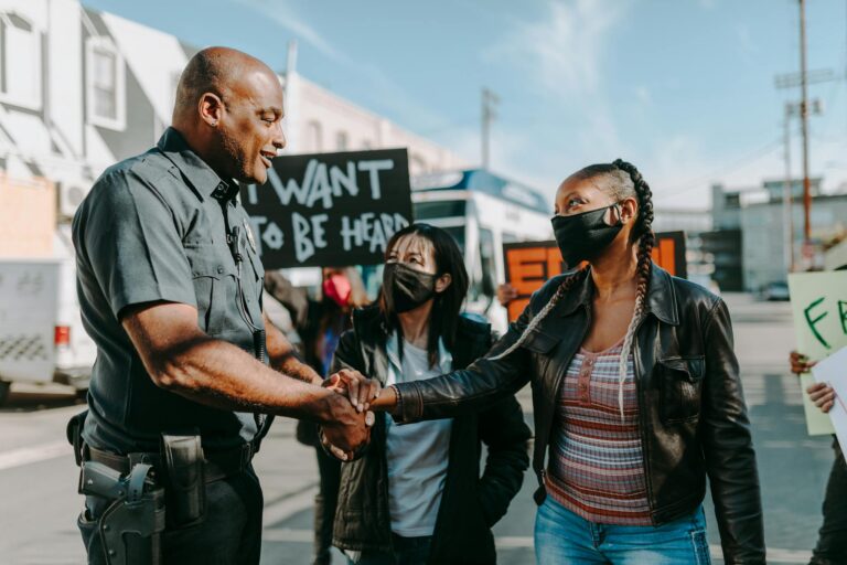 A police officer and a protester shake hands during a peaceful demonstration on a sunny day.